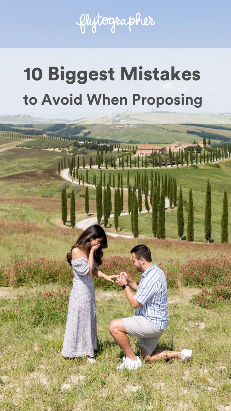 a man kneeling down next to a woman on top of a grass covered hill with trees in the background