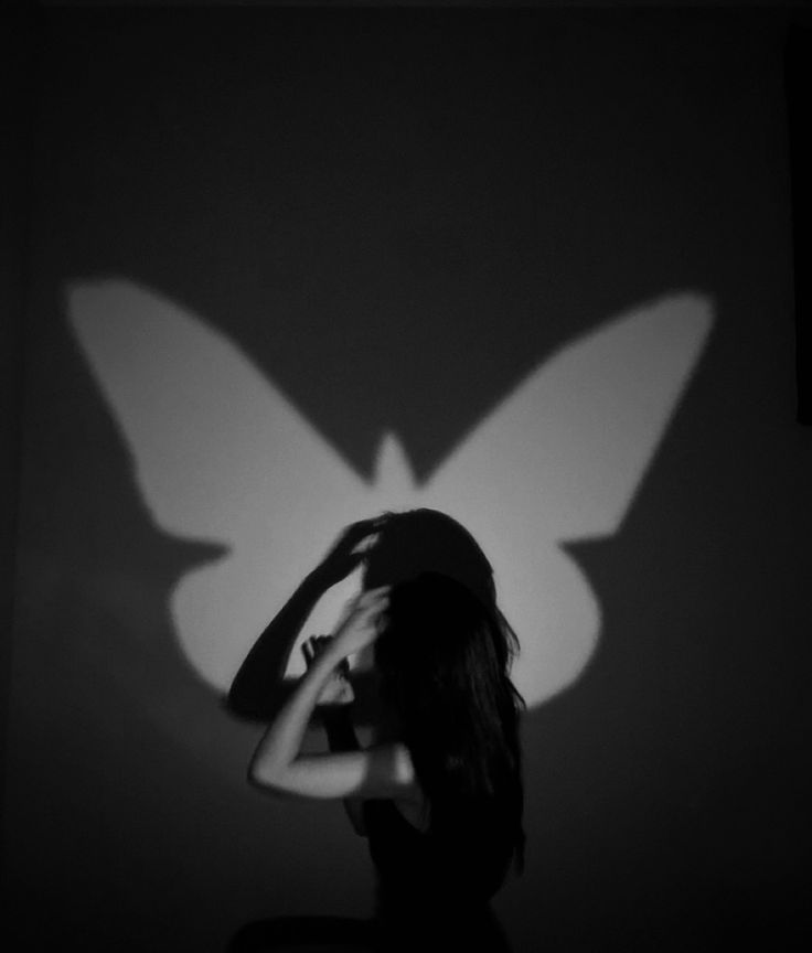 a woman standing in front of a wall with a butterfly shadow on it's back