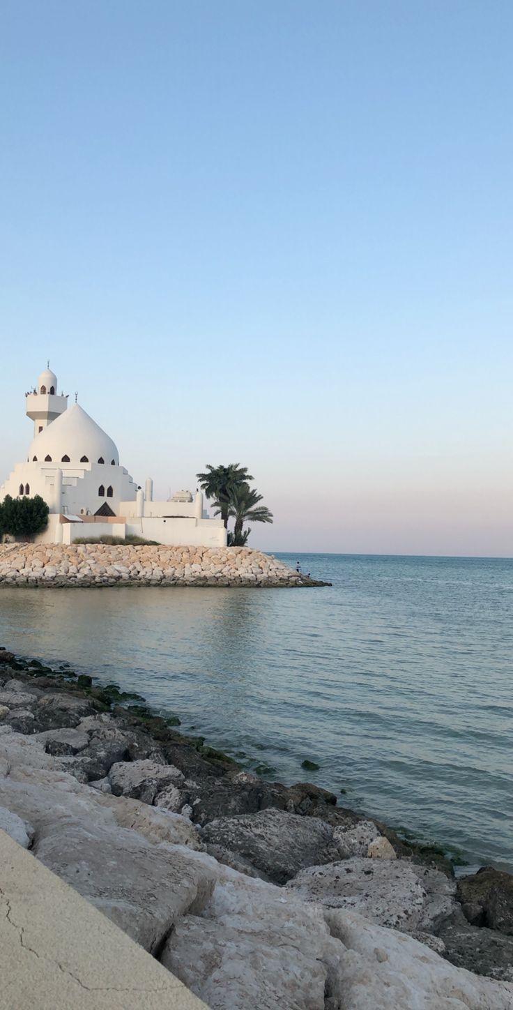 a large white building sitting on top of a beach next to the ocean with palm trees