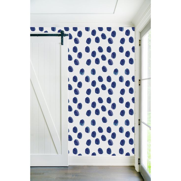 a room with white walls and blue polka dot wallpaper on the door, next to a window