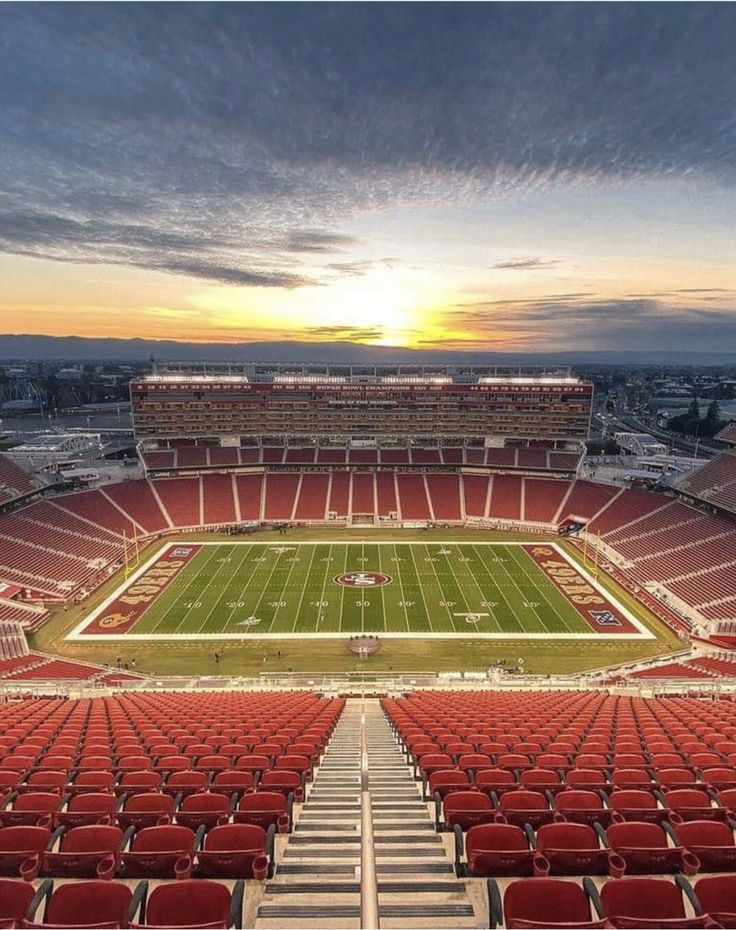 an empty football stadium with the sun setting in the background and red seats on the sidelines