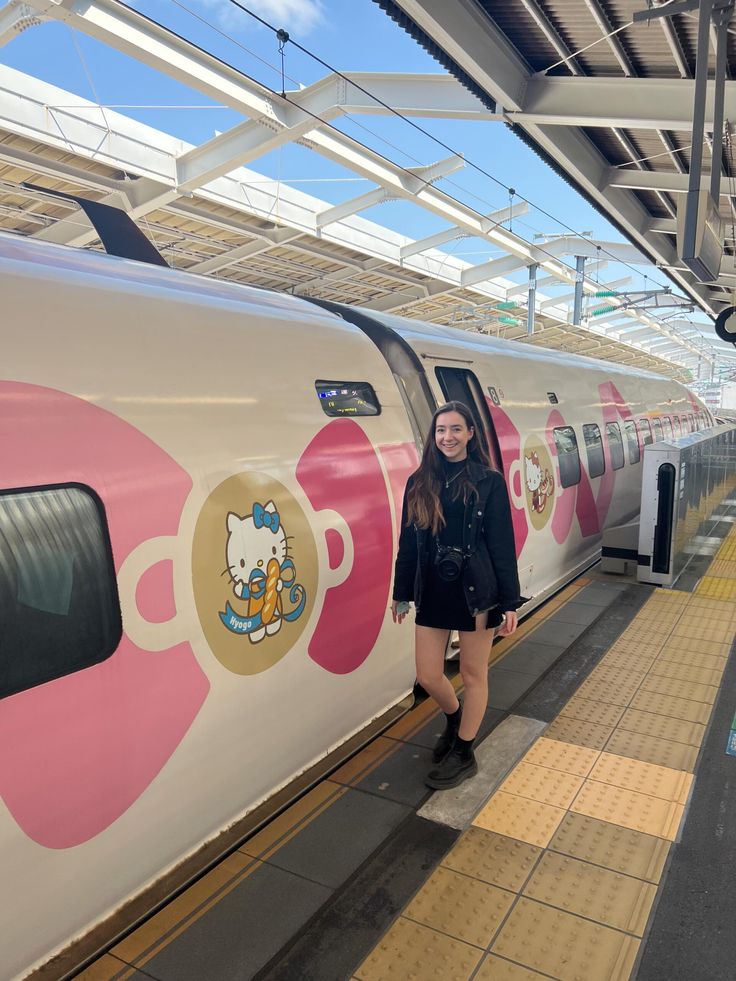 a woman standing next to a train with hello kitty stickers on it's side