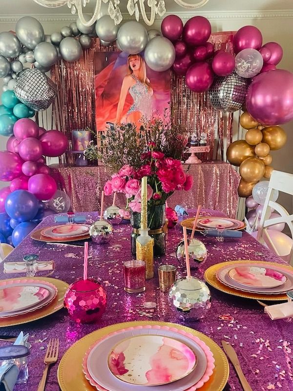 the table is set with pink and gold plates, silverware, and purple napkins