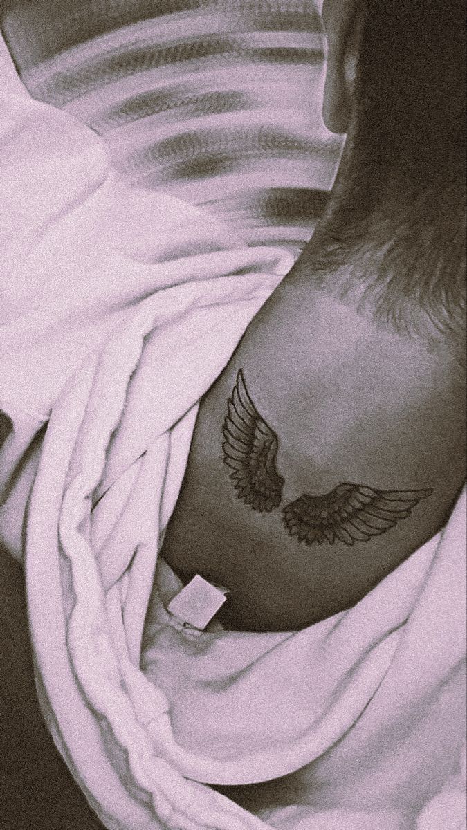 a man with a tattoo on his chest and wings around his neck, wrapped in a blanket