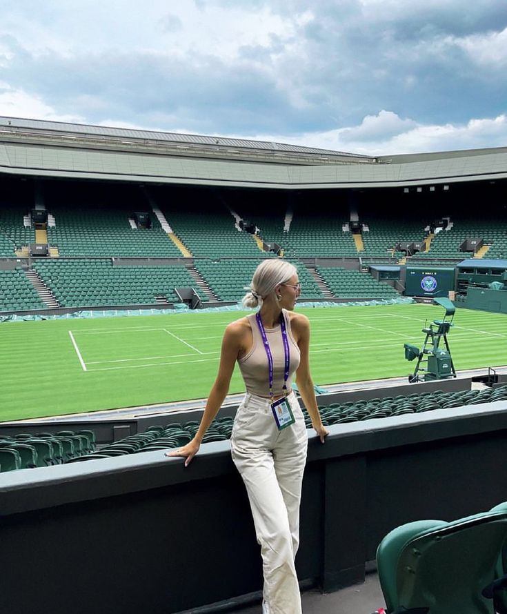 a woman standing in front of a tennis court looking out at the grass and sky