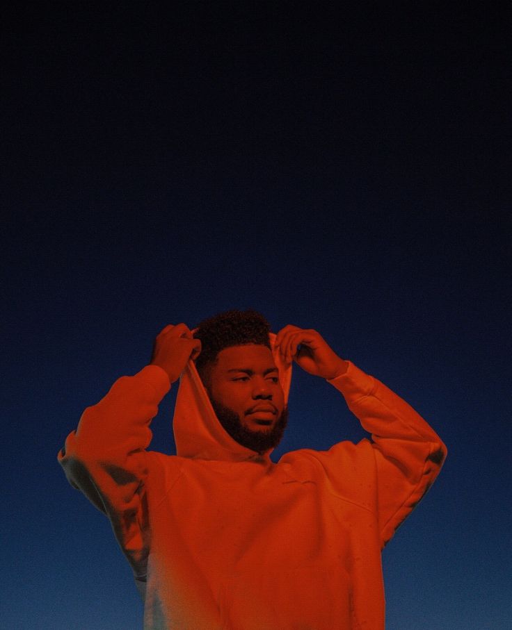 a man in an orange hoodie is holding his hands on his head and looking off into the distance