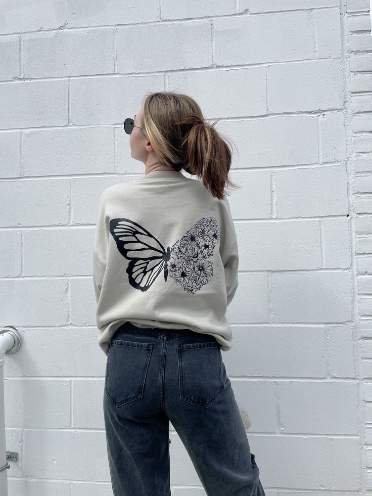 Crewneck featuring a hand drawn butterfly with blooming flowers. Makes the perfect sweatshirt to keep you warm throughout snowy days, or cool summer nights! Treat yourself while supplies last! Product Details: 90% cotton / 10% polyester Low pill, high density fabric for long lasting color Spandex ribbed cuffs and waistband for stretch Butterfly Sweatshirt, Butterfly Crewneck, Butterfly Cutout, Diy Sweatshirt, Butterfly Graphic, Butterfly Embroidery, Purple Outfits, Cute Shirt Designs, Summer Nights