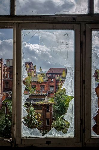 a broken glass window with buildings in the back ground and clouds in the sky behind it