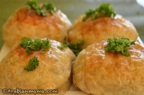 four bread rolls with parsley on top sitting on a white plate, ready to be eaten