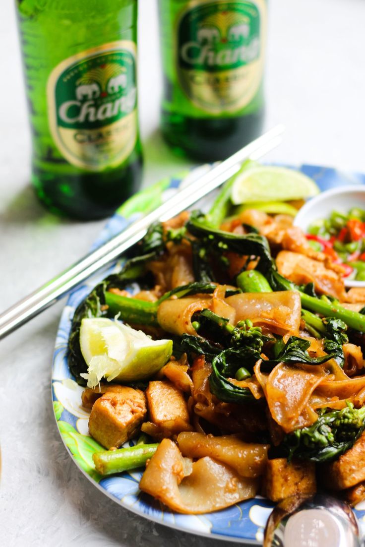 a blue and white plate topped with food next to two green beer bottles on top of a table