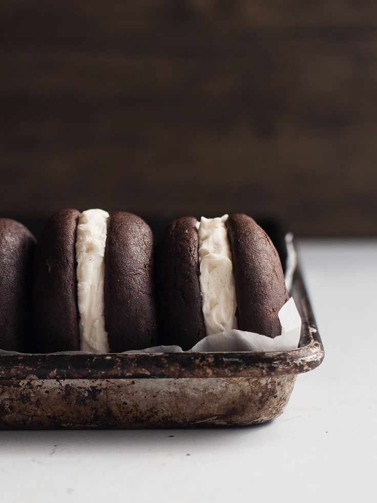 four chocolate cookies with white frosting in a tin