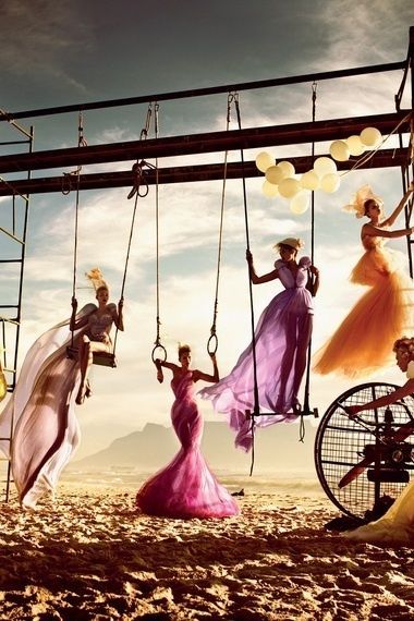 four women dressed in colorful dresses hanging from a metal structure with ladders on the beach