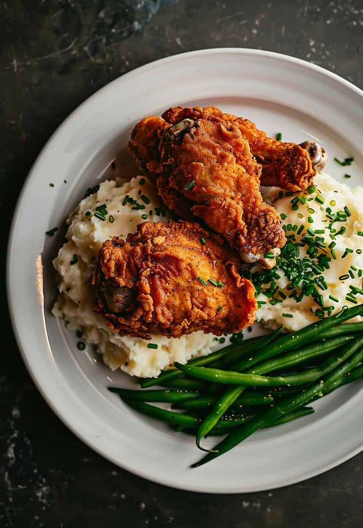 two fried chicken and mashed potatoes on a plate with green beans, garnished with parsley