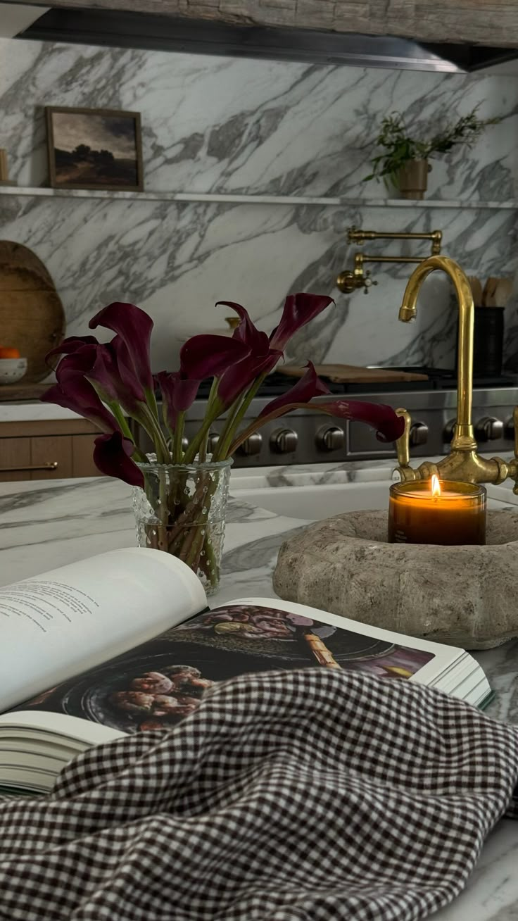 an open book sitting on top of a counter next to a candle and some flowers