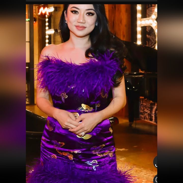 a woman in a purple dress standing next to a piano and looking at the camera