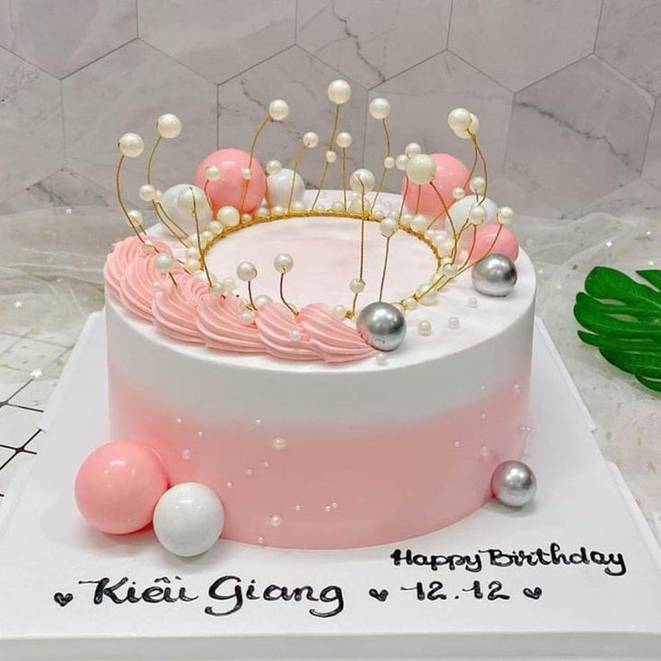 a pink and white birthday cake with pearls on the top, decorated with a tiara