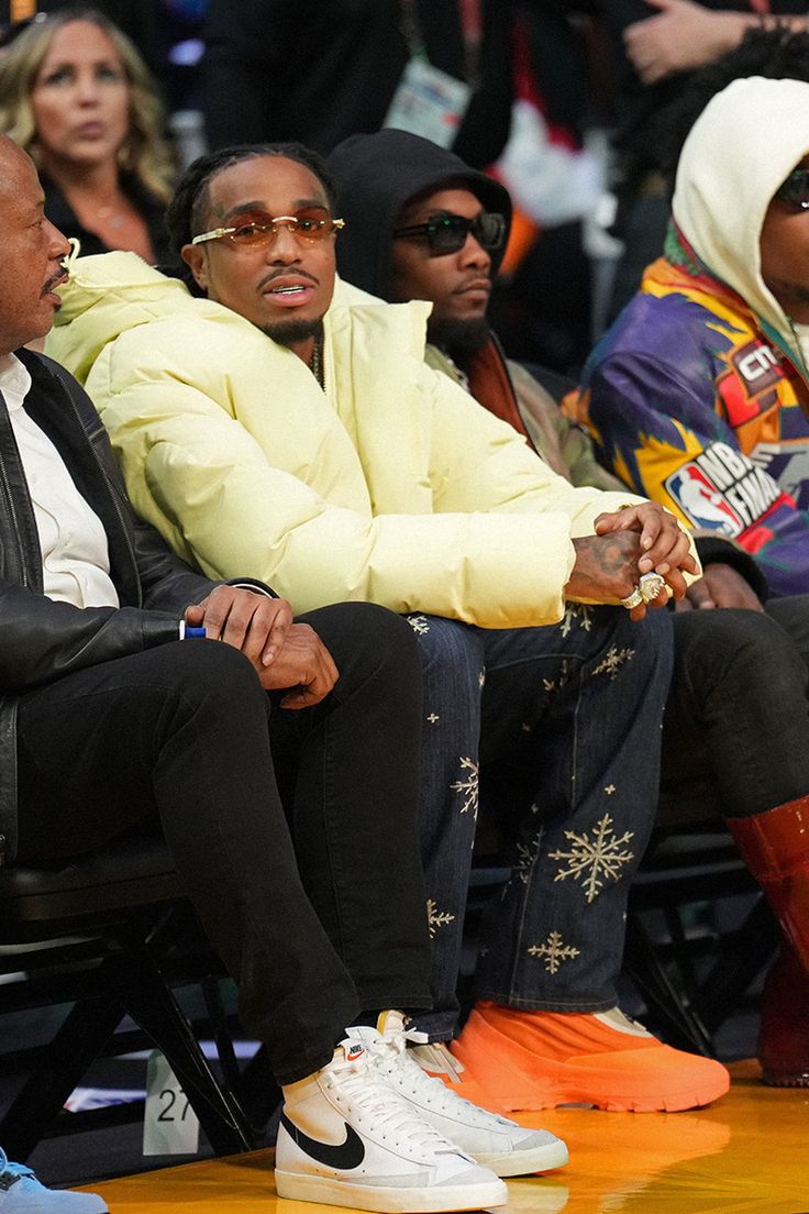 two men sitting next to each other at a basketball game, one in yellow jacket and the other in black