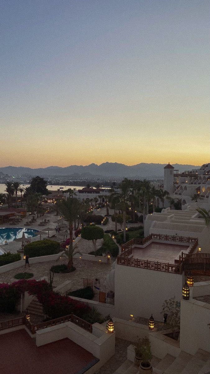 an aerial view of a resort at dusk with the sun setting in the distance and mountains in the background