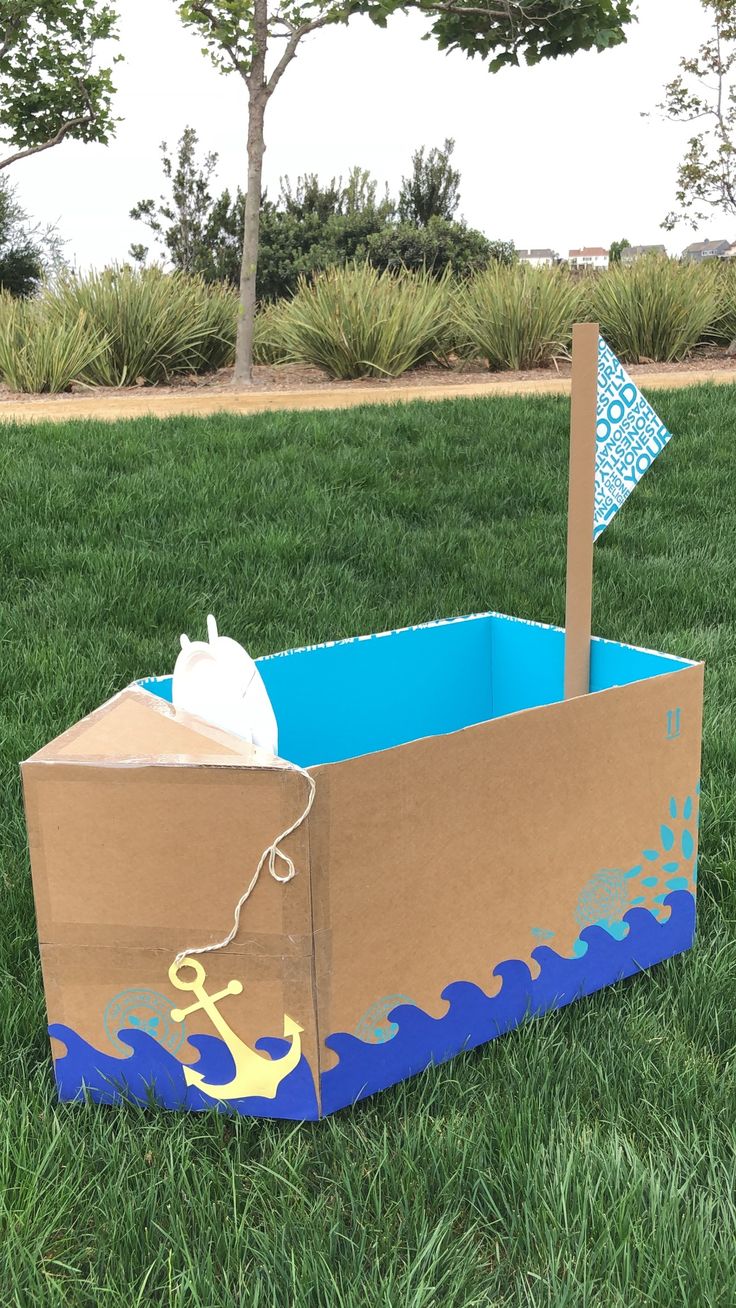 an open cardboard box sitting in the grass with a sailboat and anchor on it