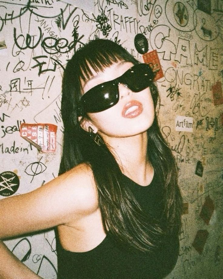 a woman with sunglasses on her head posing in front of a wall covered with graffiti