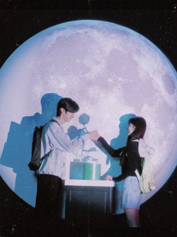 two people standing next to each other in front of a large moon with a cake on it