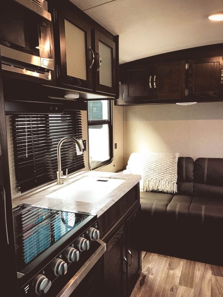 a kitchen and living room in an rv with dark wood cabinets, black leather couch, and stainless steel appliances