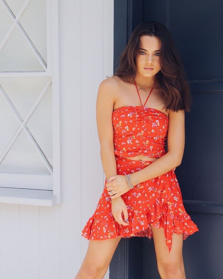 a beautiful young woman standing next to a door wearing a red dress and high heels