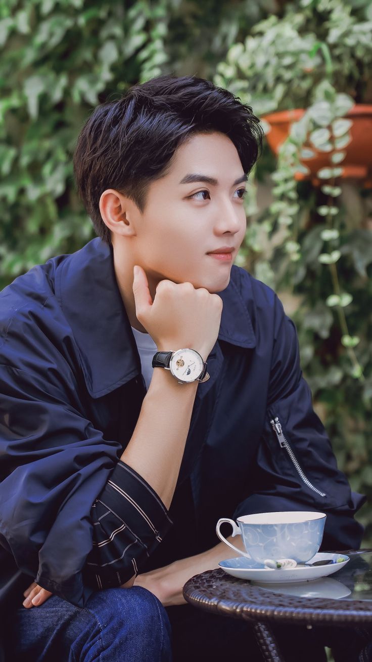 a young man sitting at a table with a cup and saucer in front of him