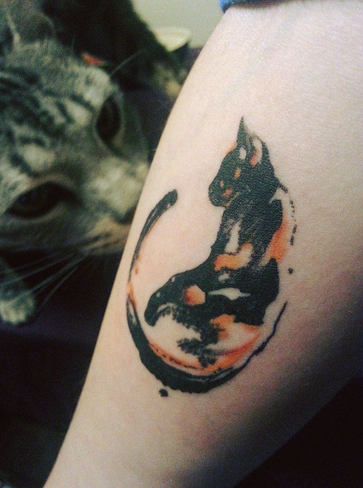 the cat is looking at the person's tattoo on her arm, which has an image of a cat in it