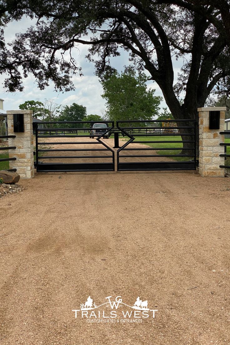 a gated entrance to a ranch with a tree in the foreground and an open field behind it