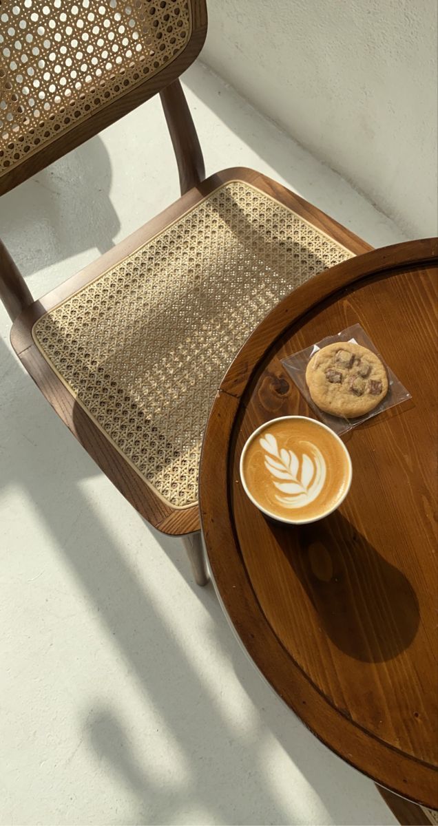 a cup of coffee sitting on top of a wooden table next to a brown chair