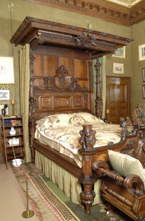 an ornate wooden bed in a bedroom with green walls and carpeted flooring, along with pictures on the wall