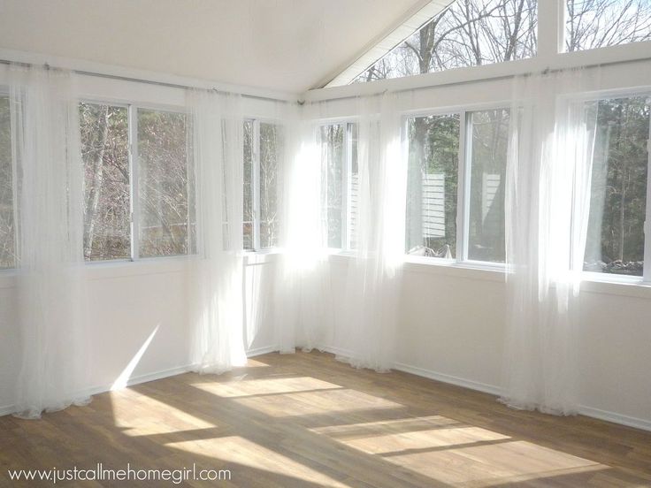 an empty room with white curtains and wood flooring is pictured in this image, the sun shines through the windows