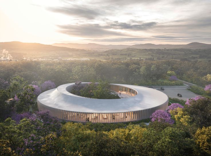 an aerial view of a circular building in the middle of trees and bushes with mountains in the background