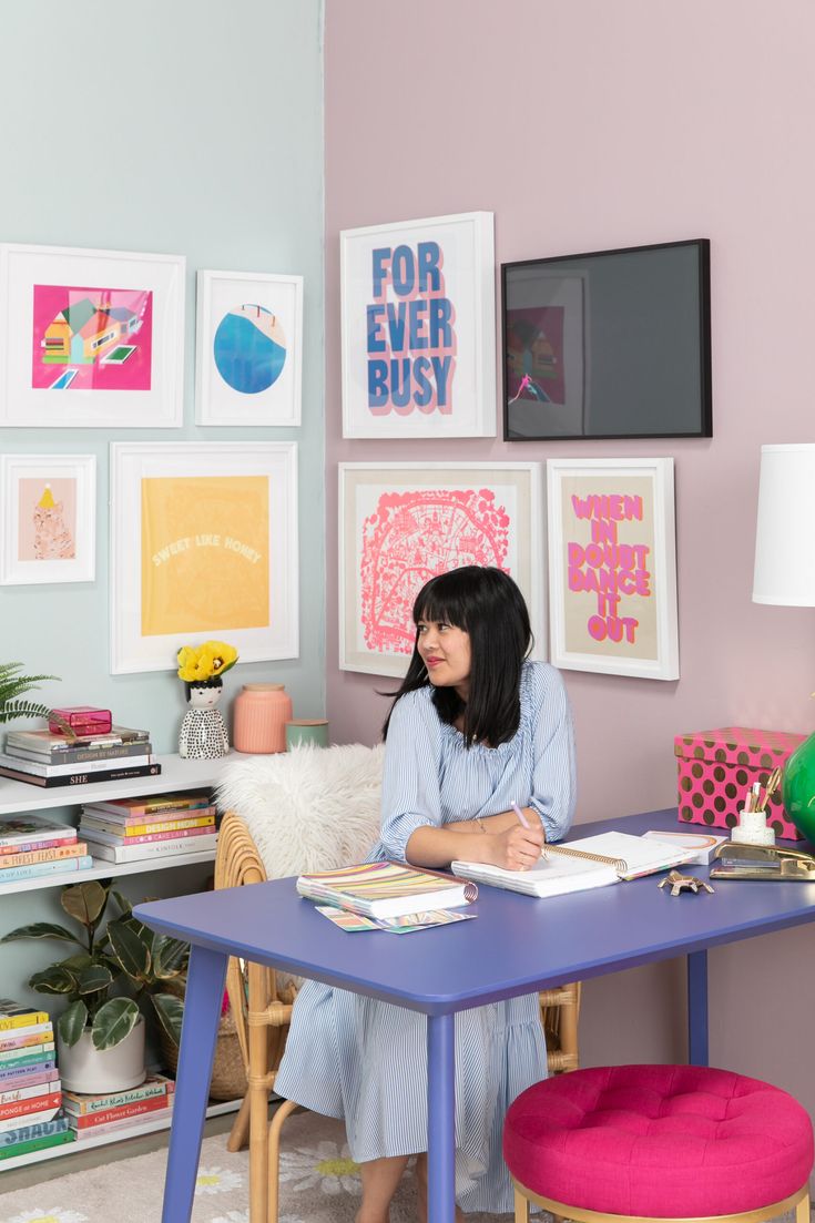 a woman sitting at a purple table in front of pictures on the wall behind her