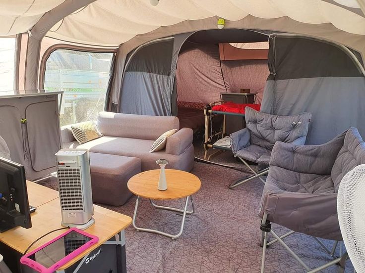 the inside of a tent with couches, chairs and televisions in front of it