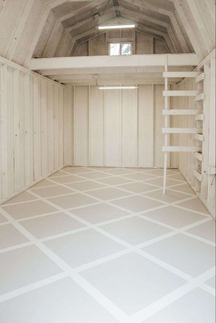 an empty storage room with white walls and floor tiles on the floor, ladders to the ceiling