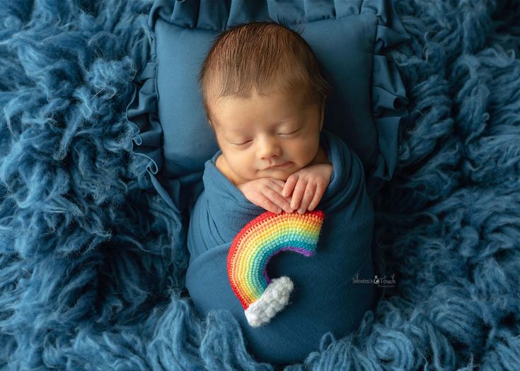 a baby laying on top of a blue blanket next to a rainbow pinwheel toy