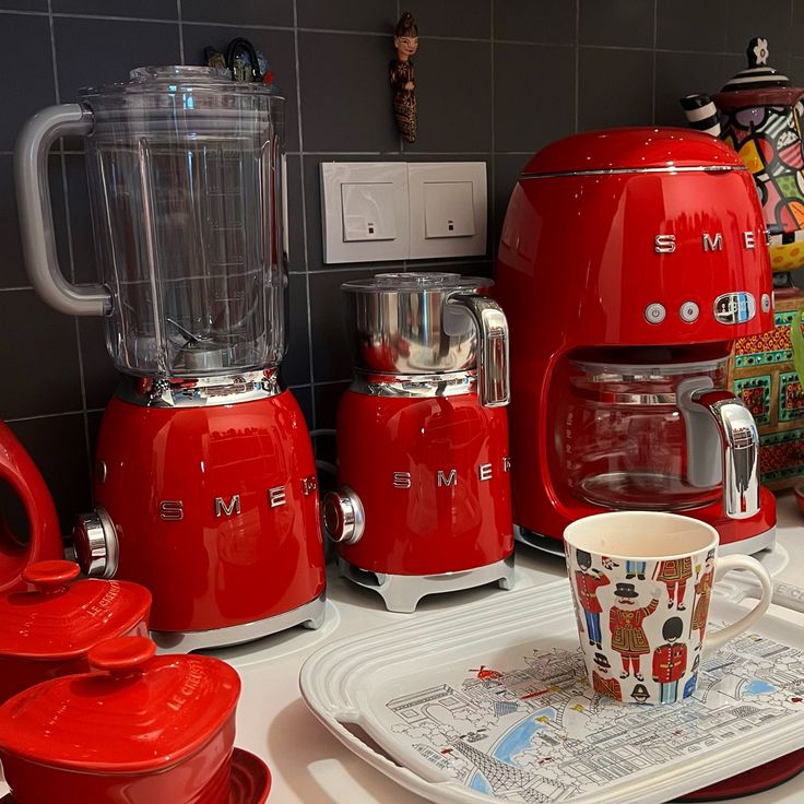 a red blender sitting on top of a counter next to a cup and saucer