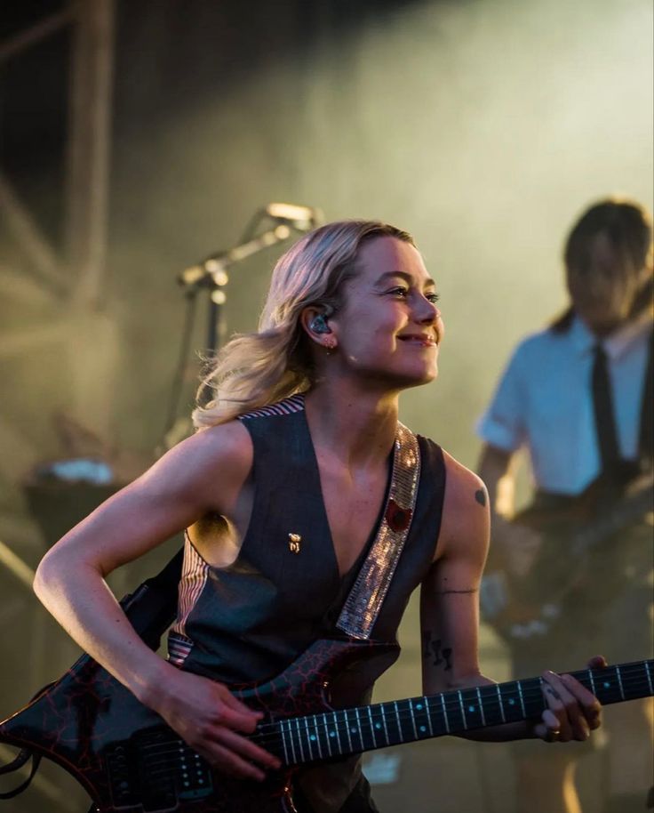 a woman holding a guitar while standing next to another person with a microphone in her hand