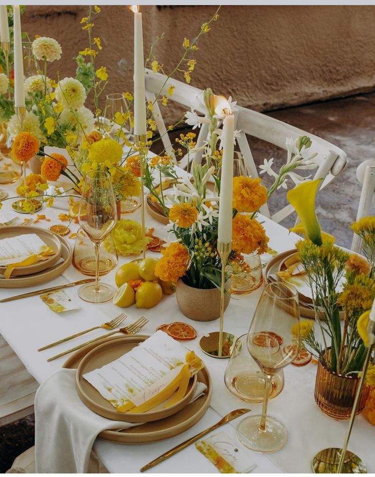 the table is set with yellow and white flowers, candles, and place settings for dinner