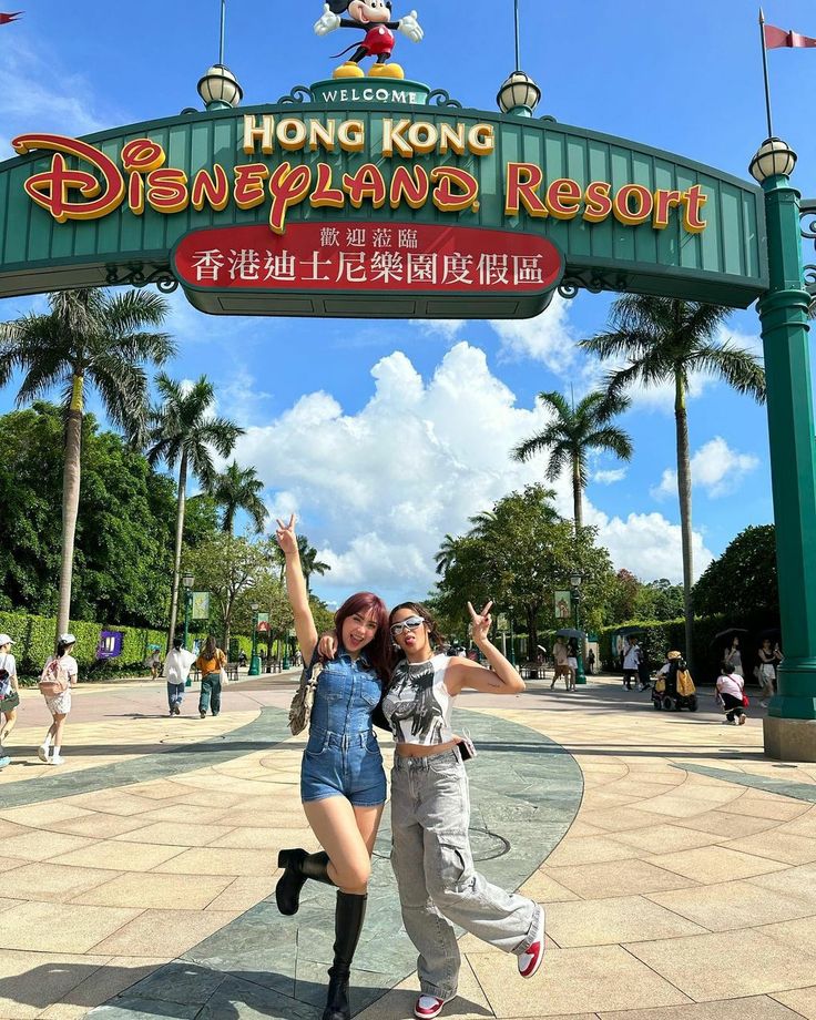 two women pose in front of the hong kong disneyland resort entrance