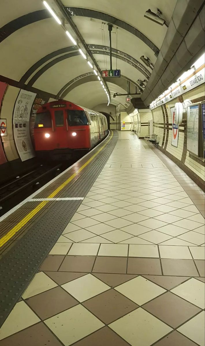 a red train is coming down the tracks in a subway station with checkered flooring