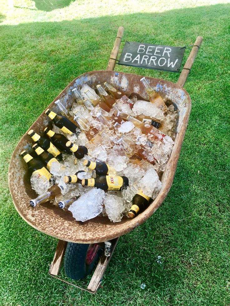 an old wheelbarrow filled with beer bottles and ice on the grass in front of a sign that says beer barrow