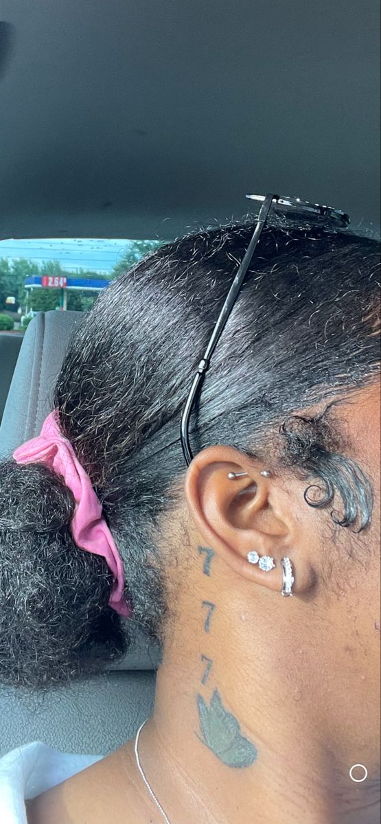 a woman with tattoos on her neck and ear sitting in a car looking out the window