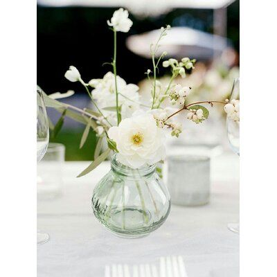 white flowers in a clear vase on a table with wine glasses and napkins around it