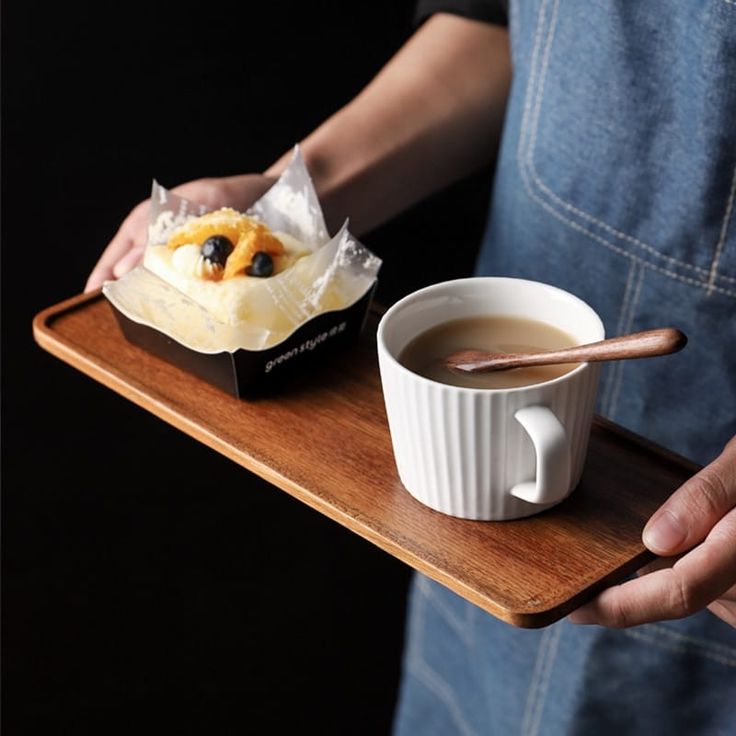 a person holding a tray with a cup of coffee and pastry on it