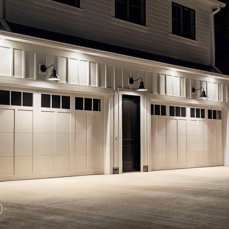 two garage doors lit up at night in front of a house with white siding and windows