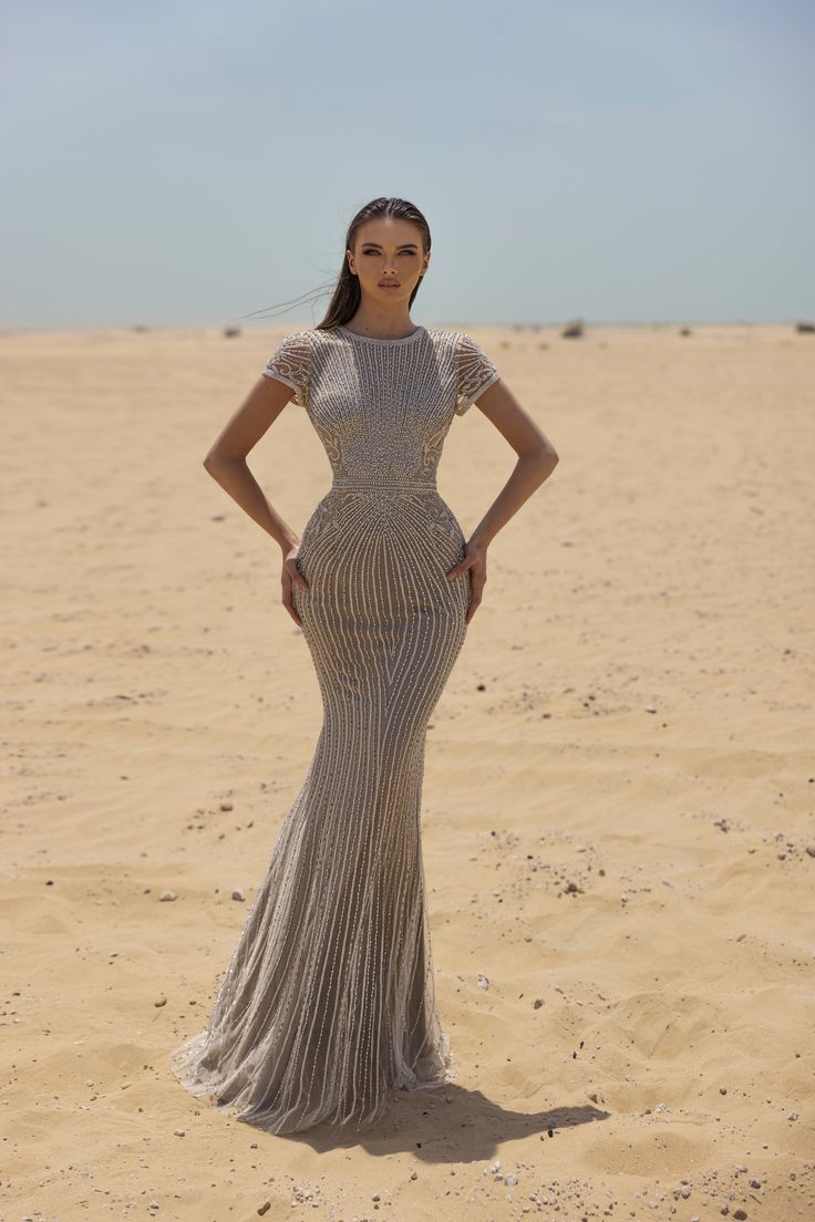 a woman standing on top of a sandy beach wearing a long silver dress and veil