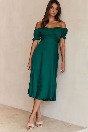 a woman in a teal dress leaning against a wall with her hands on her hips